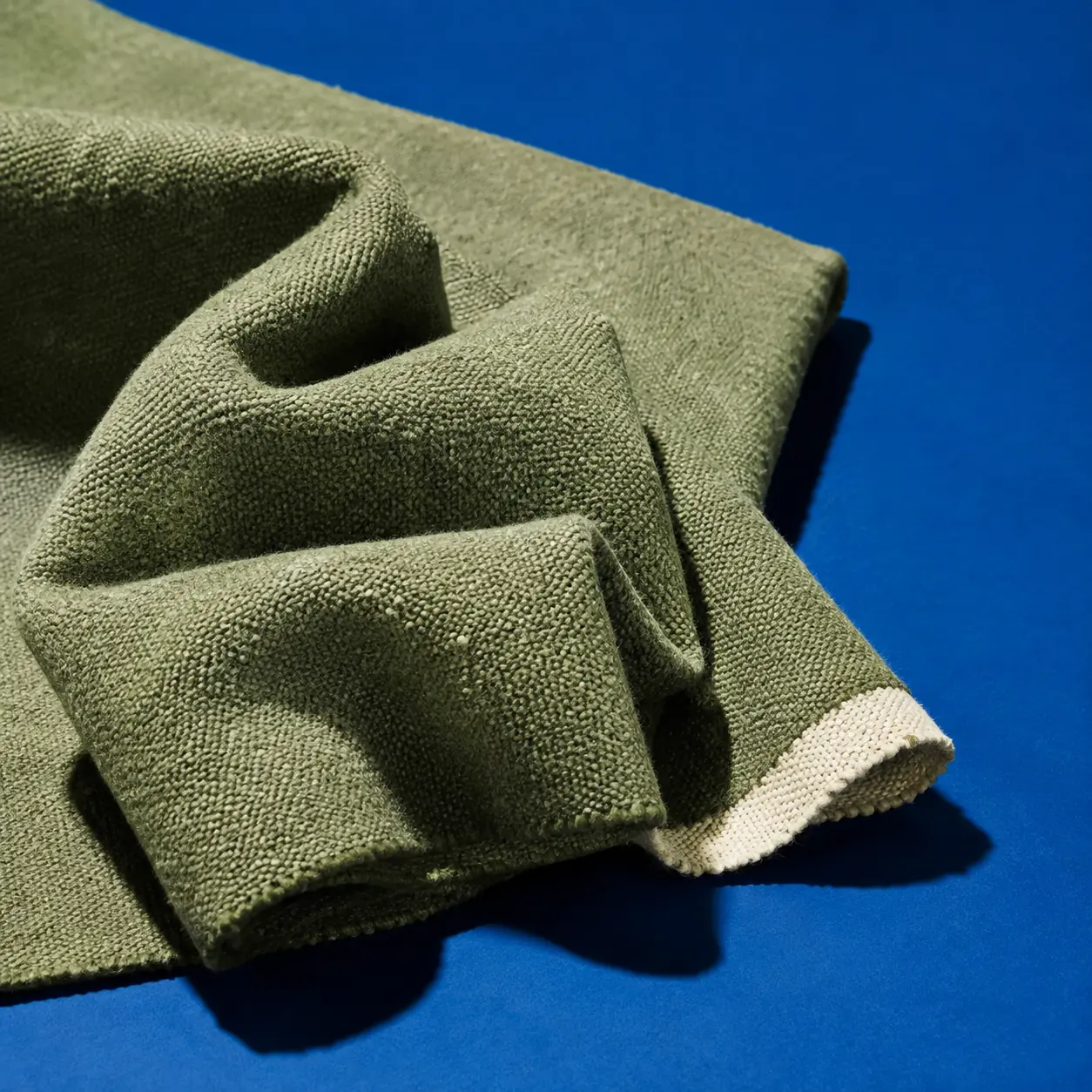 Sculptural folds of recycled sage textile on a cobalt background
